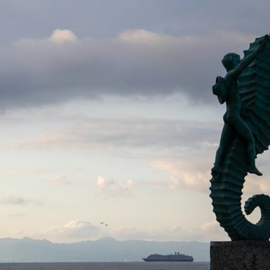 Escultura de bronce de un caballito de mar en el Malecón de Puerto Vallarta al atardecer con la bahía al fondo