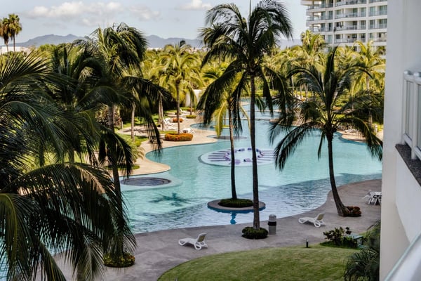 Seibal Penthouse balcony view over a resort pool and palm garden in Nuevo Vallarta