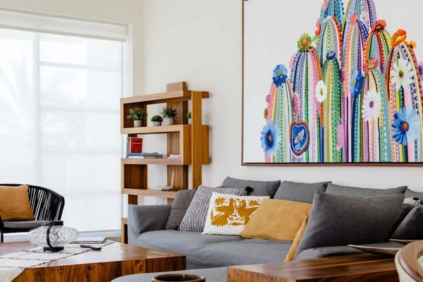 Sala de estar luminosa con sillones de madera, asientos de cuerda negra, mesa de centro de mármol, sofá gris, y estantería de madera con plantas en macetas
