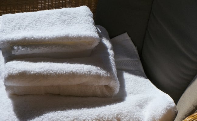 Ropa de cama y baño blanca para huéspedes, doblada en una lavandería profesional luminosa.