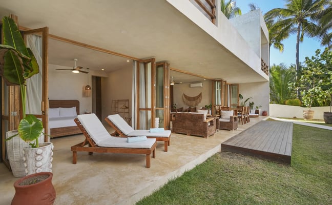 Sala de estar de concepto abierto que conecta el interior y el exterior en Villa Chukum, con muebles de mimbre, materiales naturales y vistas al mar al fondo